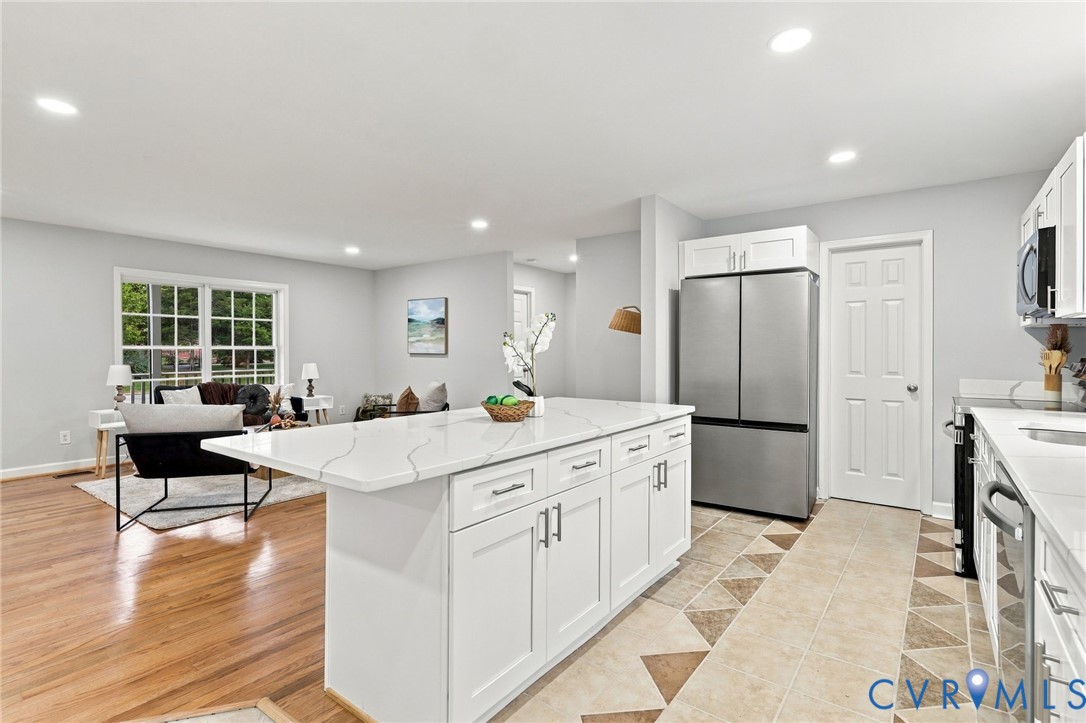 Kitchen featuring an oversized central island with white cabinetry and stone-surface countertop, stainless steel appliances, recessed ceiling lighting, and wood-finish flooring Kitchen featuring an oversized central island with white cabinetry and stone-surface countertop, stainless steel appliances, recessed ceiling lighting, and wood-finish flooring
