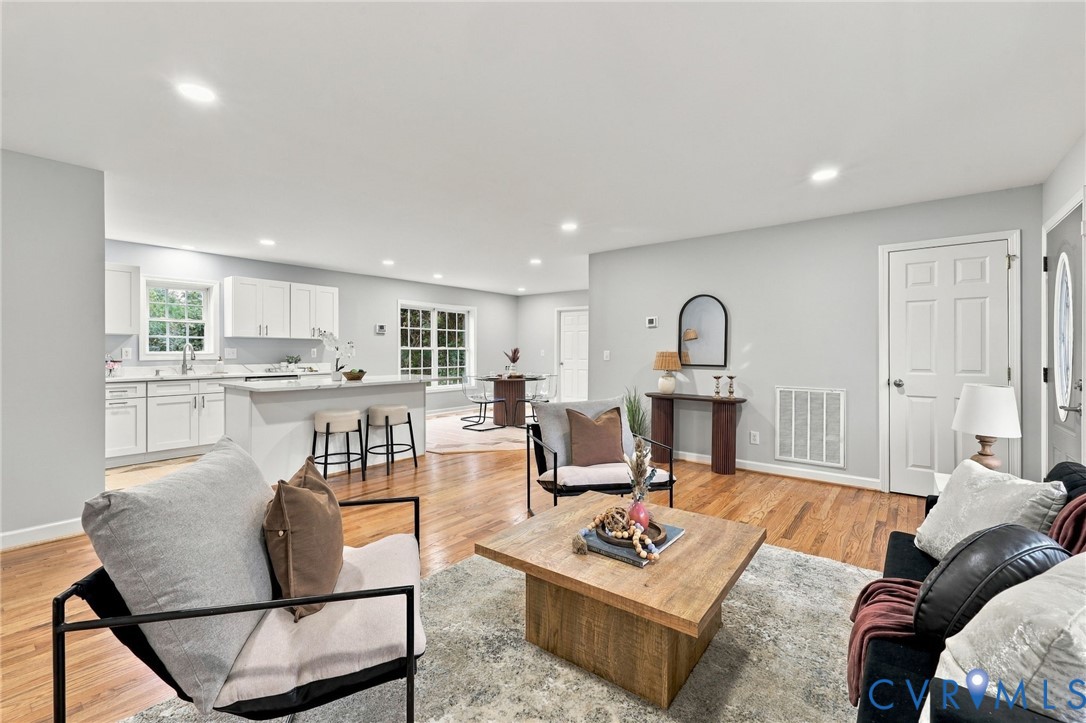 Open-concept floor plan featuring wood-finish flooring, recessed lighting, white cabinetry, and an eat-in kitchen island Open-concept floor plan featuring wood-finish flooring, recessed lighting, white cabinetry, and an eat-in kitchen island