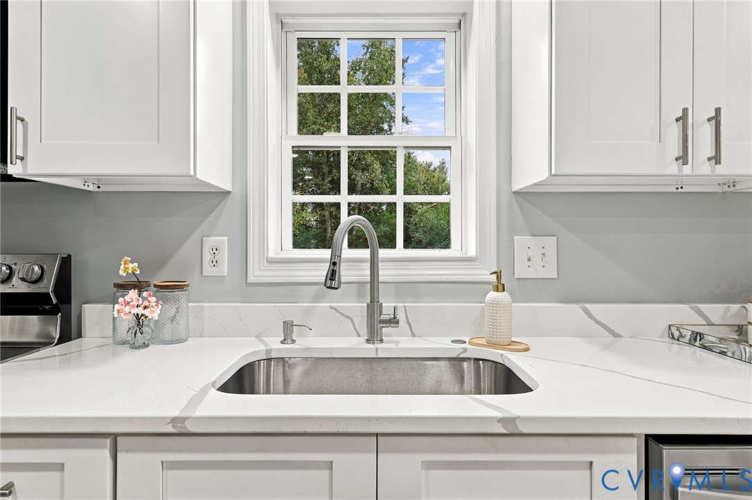 Kitchen area featuring white shaker-style cabinetry, quartz countertops with gray veining, an undermount stainless steel sink, a pull-down stainless steel faucet, and a multi-pane window