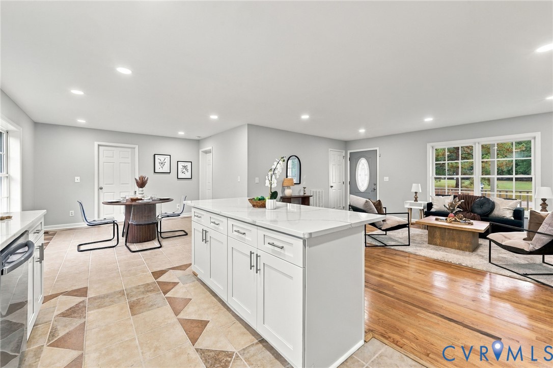 Open-concept interior featuring white cabinetry with stone-finish countertops, a central kitchen island, wood-finish flooring, multi-pane windows, and recessed lighting