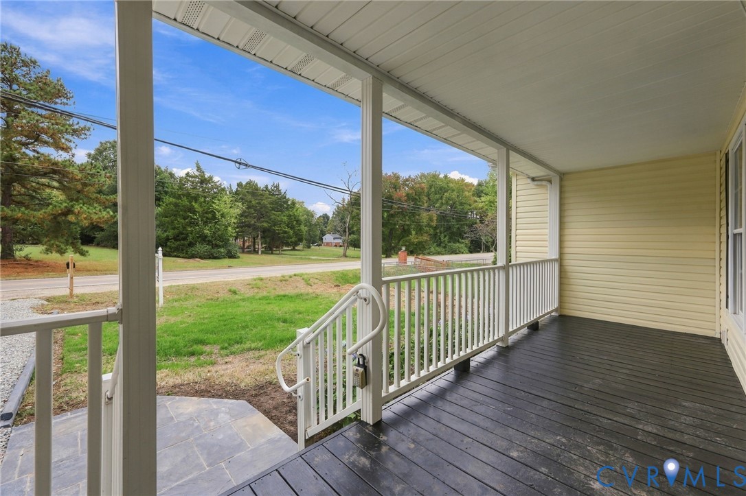 Covered front porch featuring dark-toned wood-finish flooring, white railing, and a stone walkway