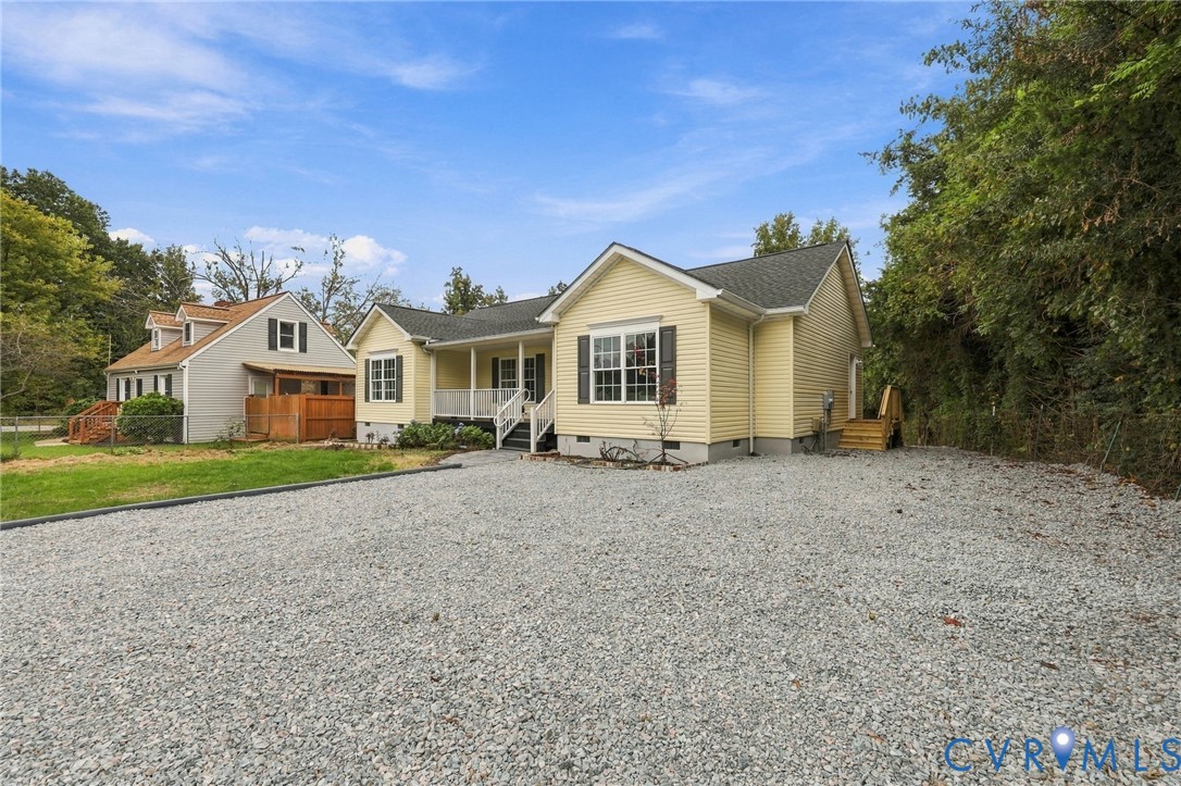 Single-story residence featuring light-colored horizontal lap siding, a front covered porch with railings, and a gravel driveway