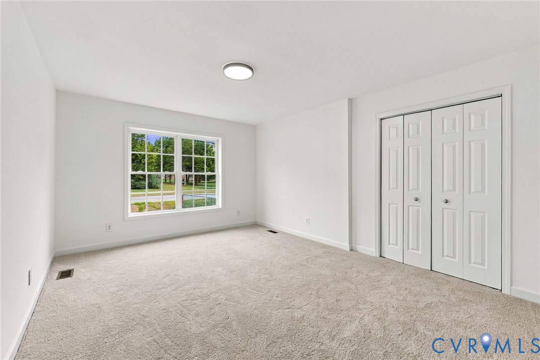 Neutral-toned carpeting, crisp white walls, large grid-pane window, and four-panel bi-fold closet doors