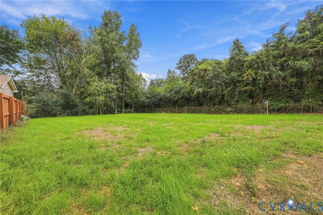 Expansive grassy lot featuring a wood fence and perimeter of mature trees