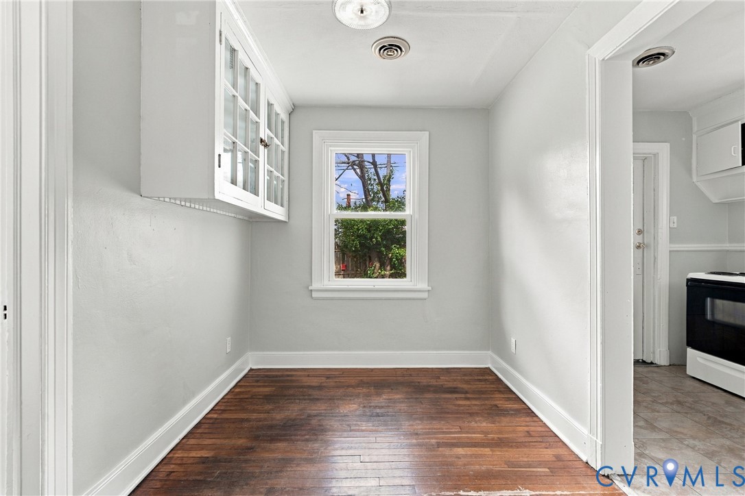 Bright hallway with warm wood-finish flooring, white painted walls, and abundant natural light from a large window