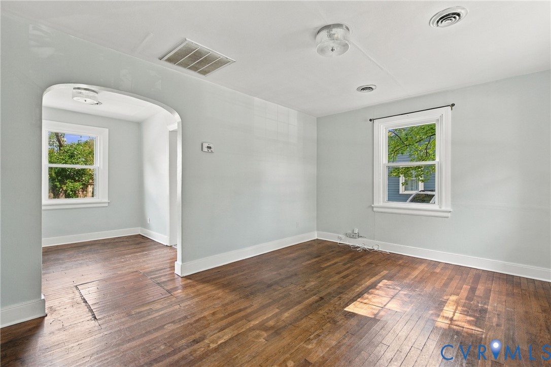 Hardwood flooring, painted walls, white trim, arched doorway, and ceiling-mounted light fixtures