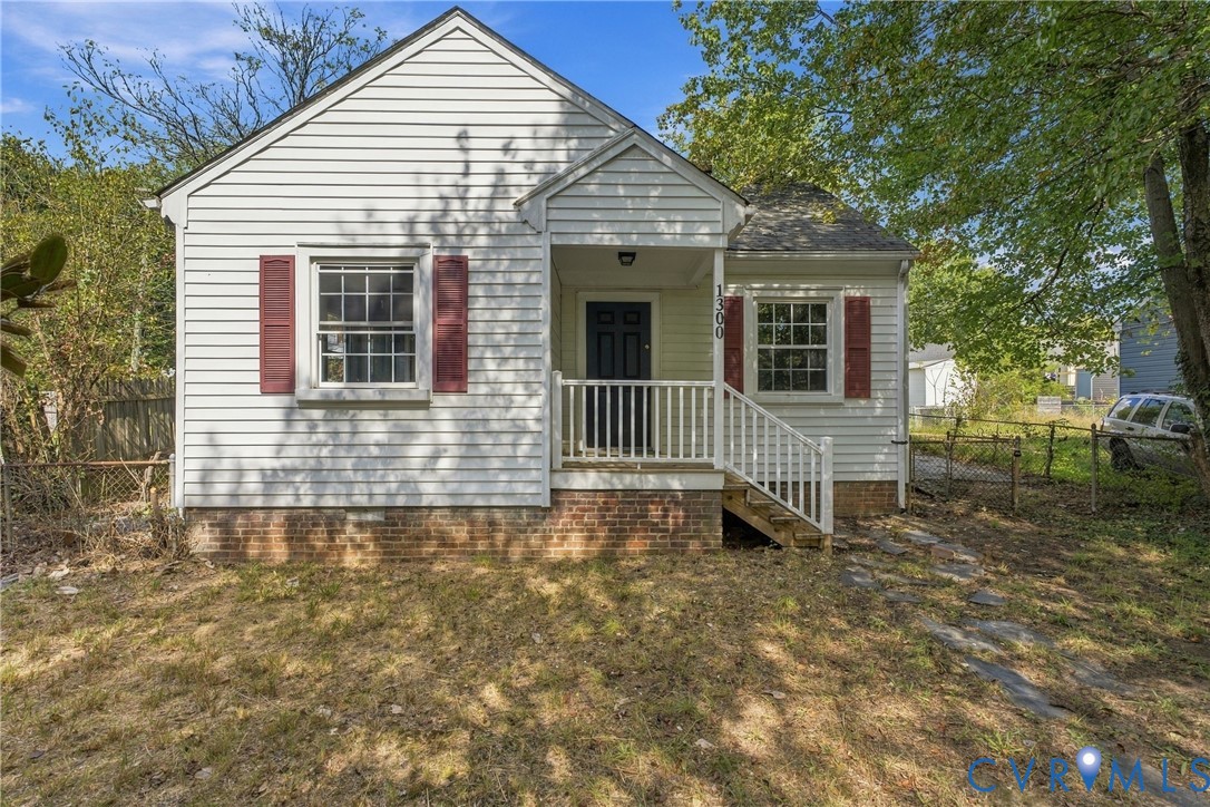 Exterior featuring horizontal white siding, red window shutters, a covered front porch with white railings, and a dark front door Exterior featuring horizontal white siding, red window shutters, a covered front porch with white railings, and a dark front door