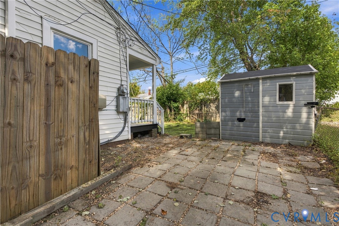 Paved patio area, wood privacy fence, exterior storage shed, white siding, and a rear porch
