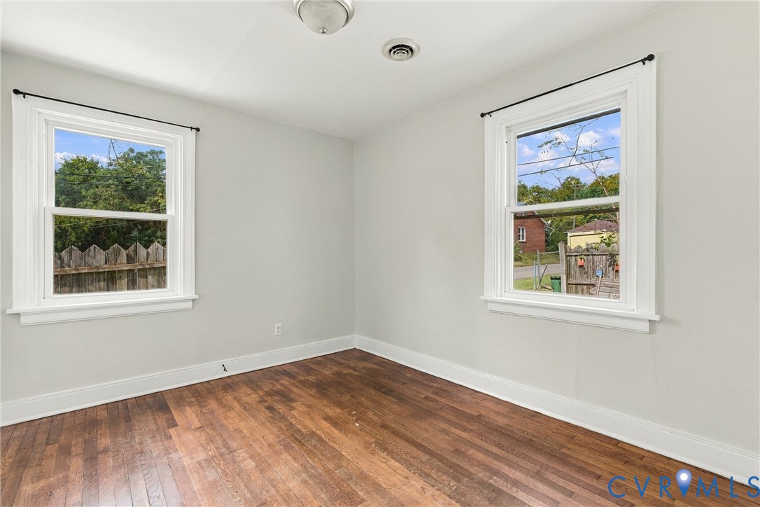 Bright, light-filled room showcasing gleaming wood-finish flooring, two large double-hung windows with white trim and black hardware, crisp white walls, and recessed ceiling lighting
