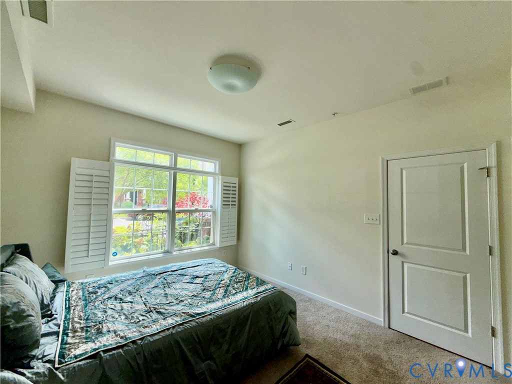 Bright interior space featuring a large window with white plantation shutters, carpeted flooring, and a flush-mount ceiling light fixture