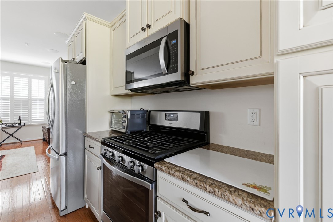 Stainless steel appliances, gas range, wood-finish flooring, white cabinetry, and plantation shutters
