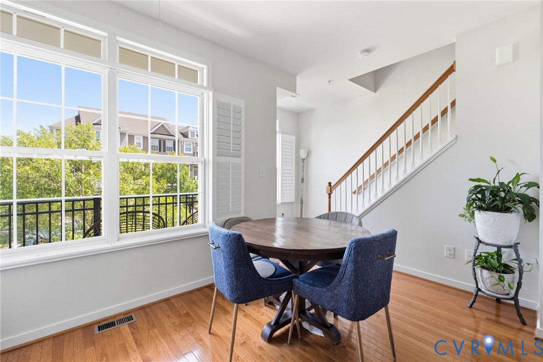 Hardwood-style flooring throughout, large windows with white louvered shutters, and a staircase with a wood-finish handrail and white balusters