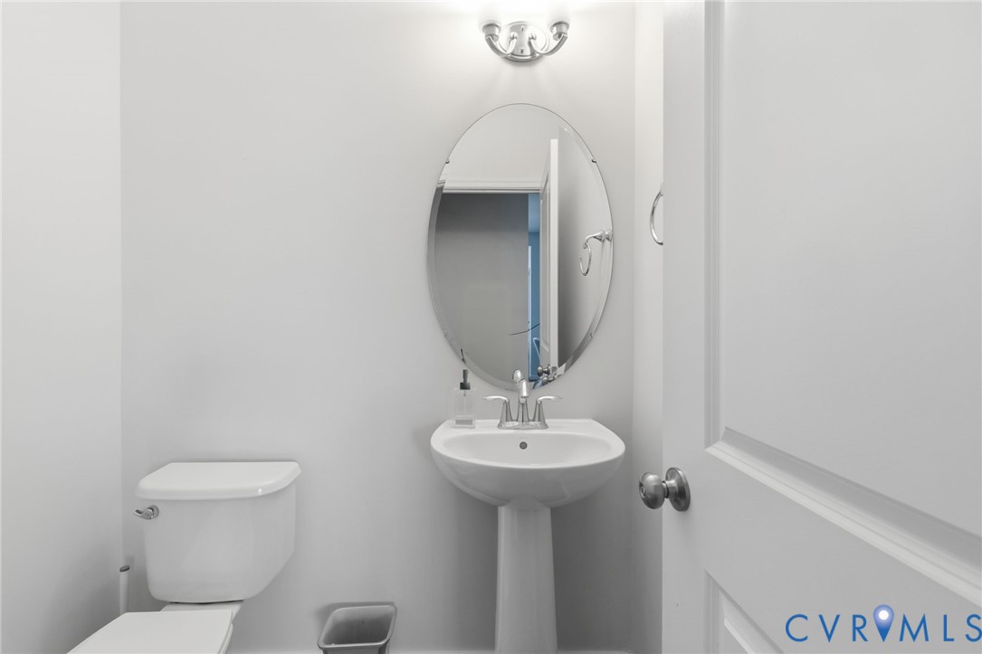 Pedestal sink with chrome-finish faucet, oval mirror, wall-mounted light fixture, and white toilet