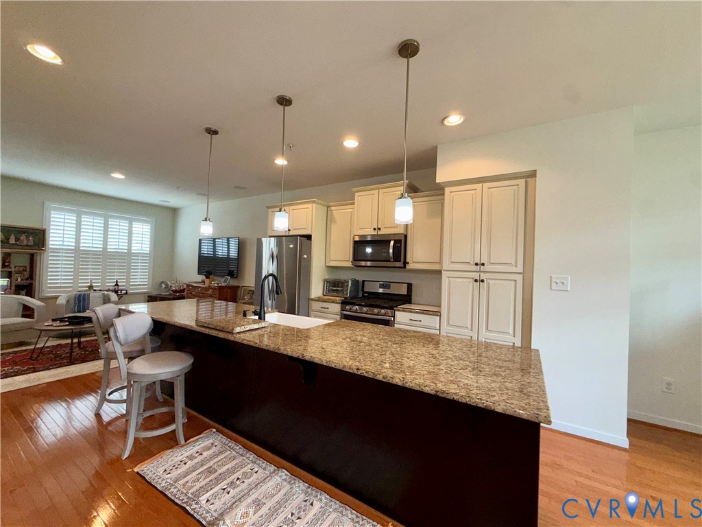Open-concept kitchen featuring an expansive island with a granite countertop, white shaker cabinetry, stainless steel appliances, and recessed lighting