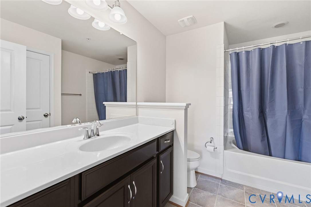Bathroom featuring a single vanity with dark wood-finish cabinetry, a white countertop with an integrated sink, a large wall mirror, and a shower-over-tub combination with white tile surround