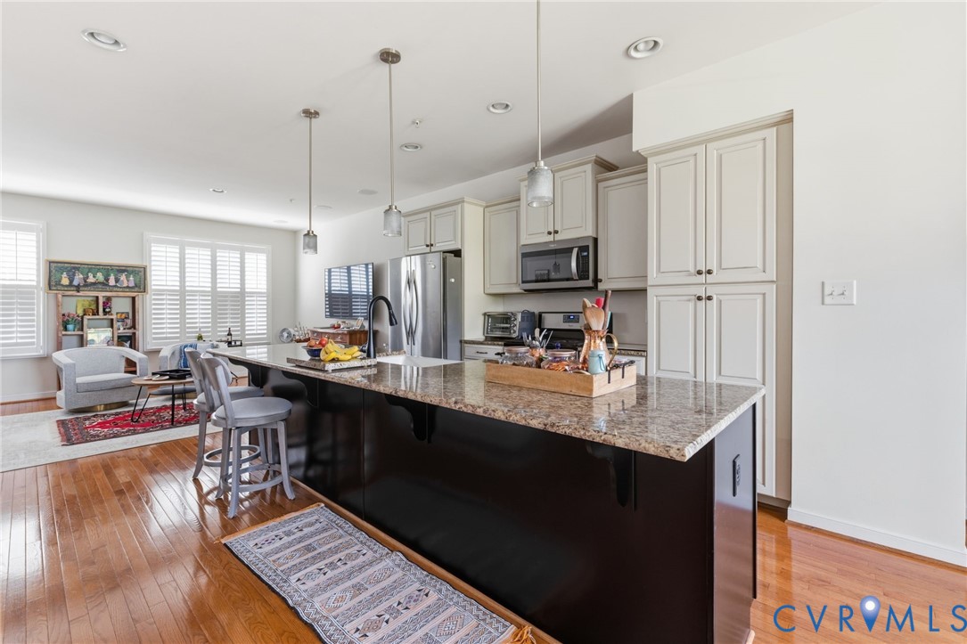 Spacious kitchen featuring a large island with a stone countertop, light-toned cabinetry, stainless steel appliances, and recessed lighting