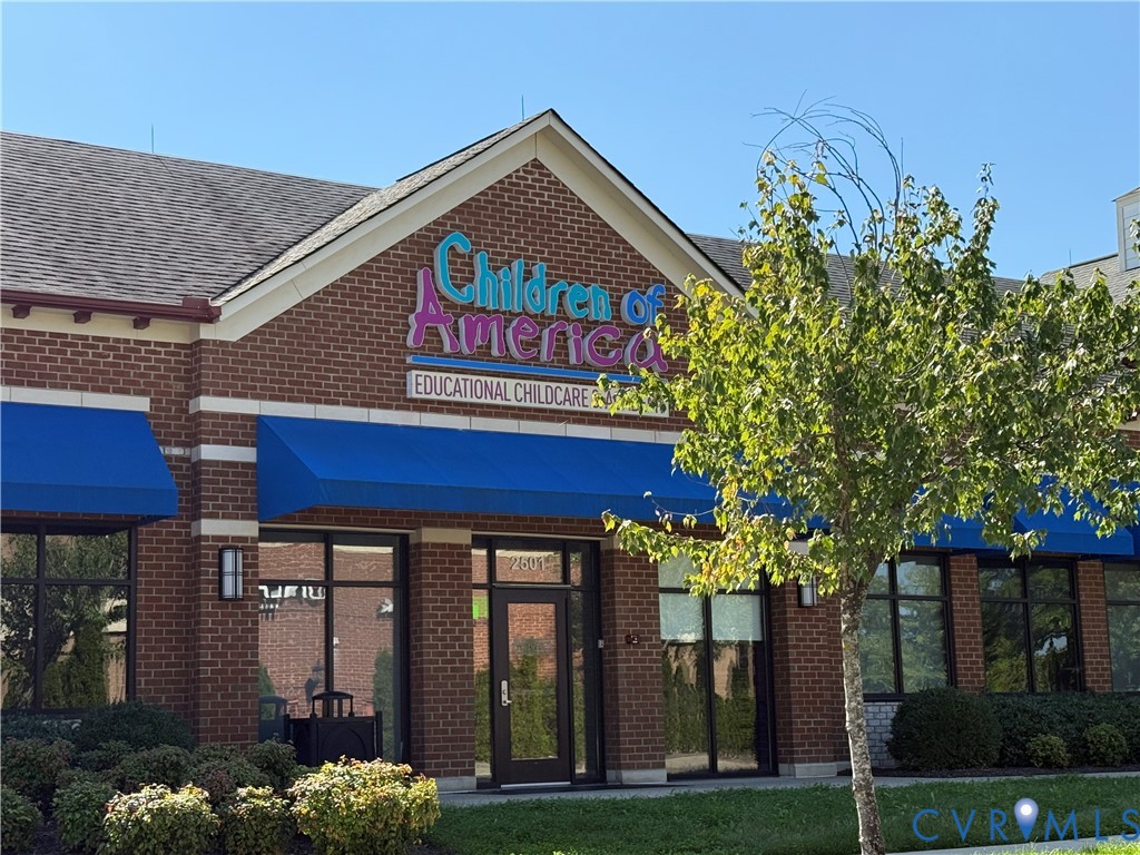 Brick exterior with a gabled roofline, multiple windows, blue awnings, and landscaping