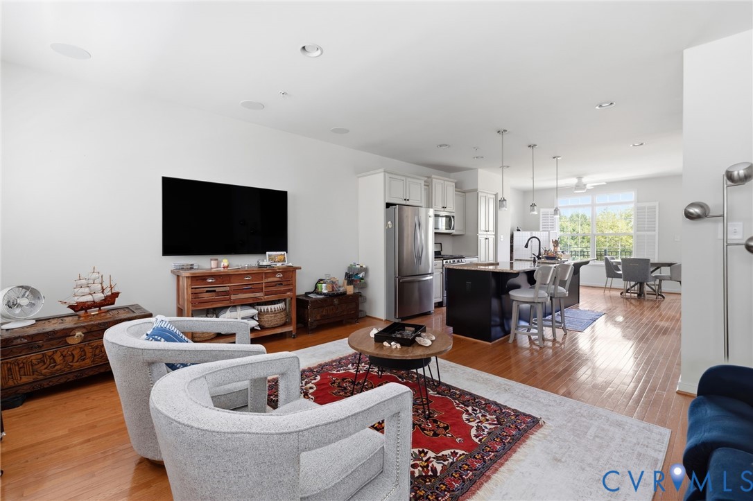Hardwood flooring throughout, featuring an open-concept layout with recessed lighting, a kitchen island with pendant lighting, and stainless steel appliances