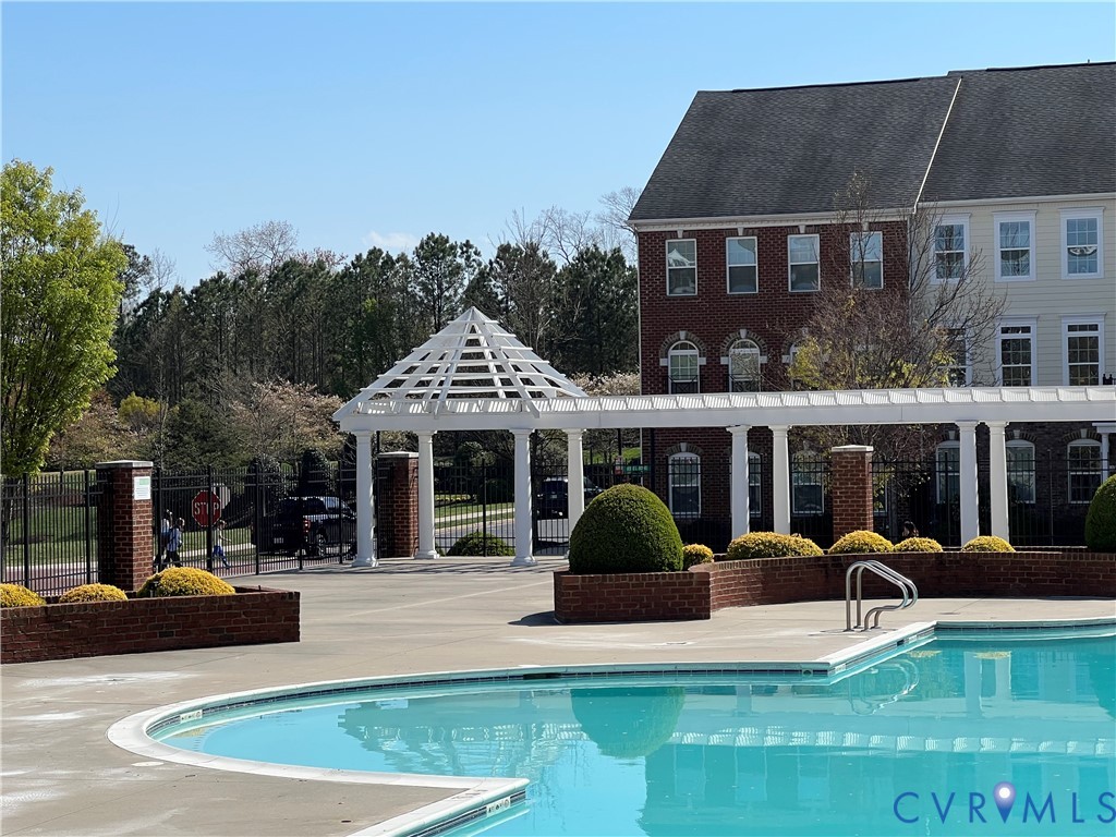 Swimming pool with curved edge, white pergola, brick accents, and mature landscaping