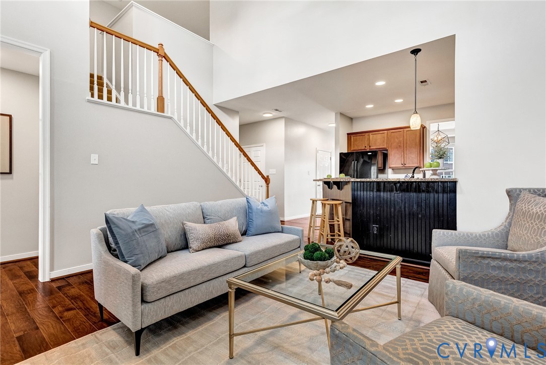 Hardwood flooring, two-story ceiling, kitchen pass-through with breakfast bar, wood cabinetry, and a staircase with wood handrail and white spindles