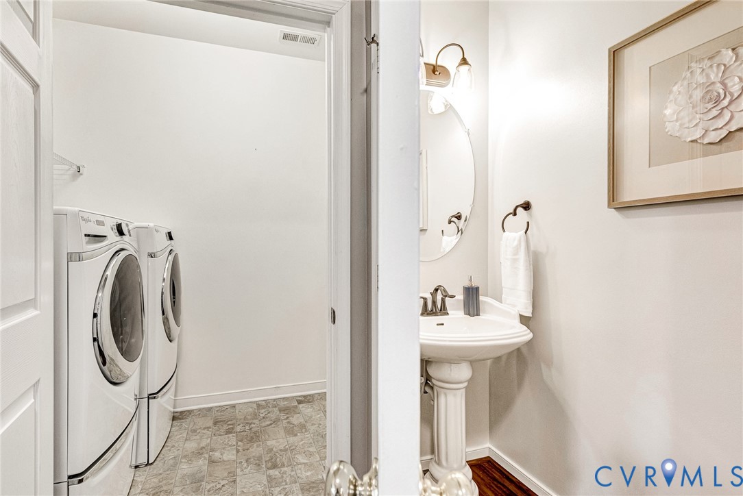 Pedestal sink with an oval mirror, wall-mounted light fixture, and dark wood-finish flooring