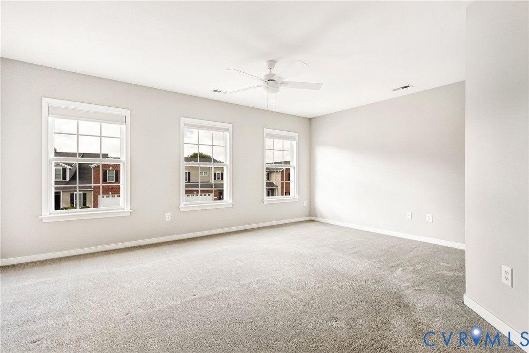 Bright room with three double-hung windows, light-toned carpeting, and a ceiling fan