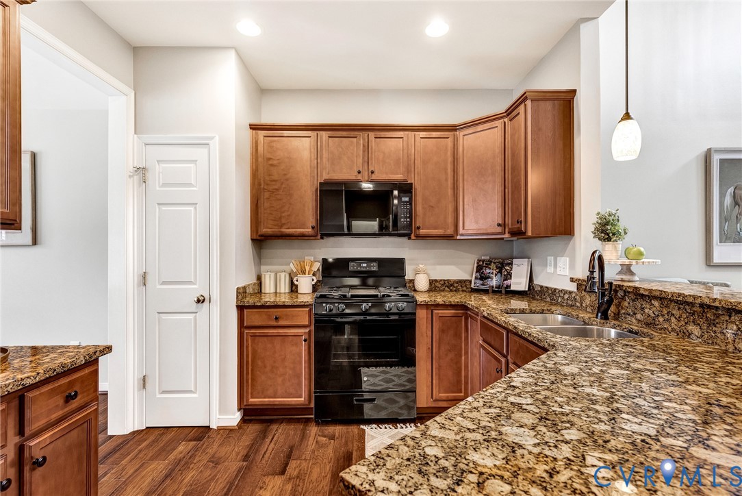 Kitchen featuring wood-finish flooring, rich wood cabinetry, stone countertops, a stainless steel double sink, and black appliances Kitchen featuring wood-finish flooring, rich wood cabinetry, stone countertops, a stainless steel double sink, and black appliances