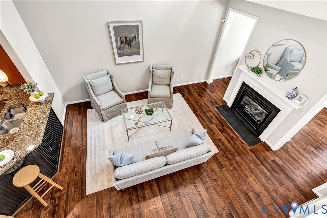 Vaulted ceiling enhancing vertical space, wood-finish flooring throughout, built-in fireplace with a white mantel, kitchen counter with an integrated sink, and an elevated counter