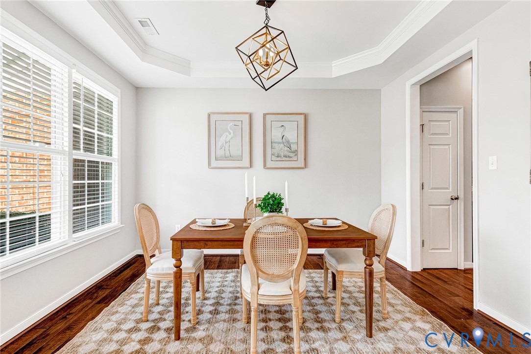 Tray ceiling with crown molding, geometric pendant light fixture, multiple windows with blinds, and rich wood-finish flooring Tray ceiling with crown molding, geometric pendant light fixture, multiple windows with blinds, and rich wood-finish flooring
