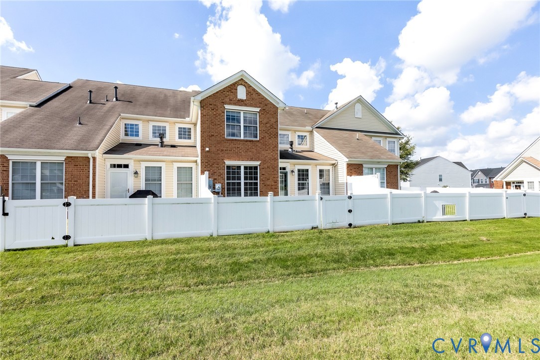 Rear exterior featuring brick and siding finishes, multiple windows, a white privacy fence, and a green lawn