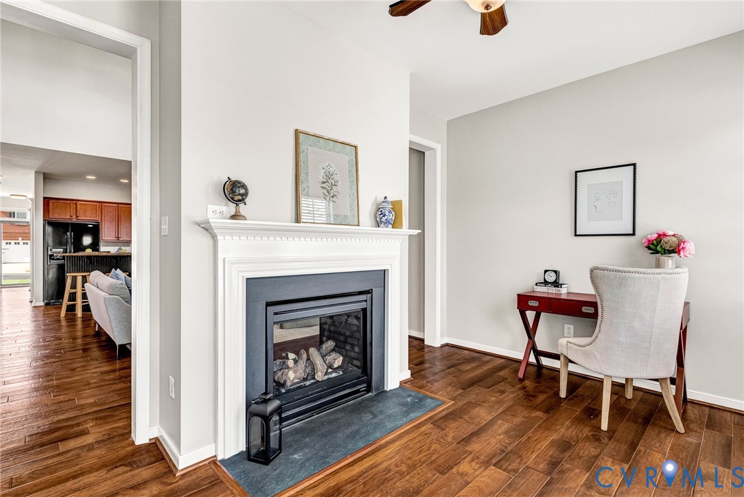 Wood-finish flooring throughout, a gas fireplace with a classic white mantel, and a ceiling fan with integrated lighting