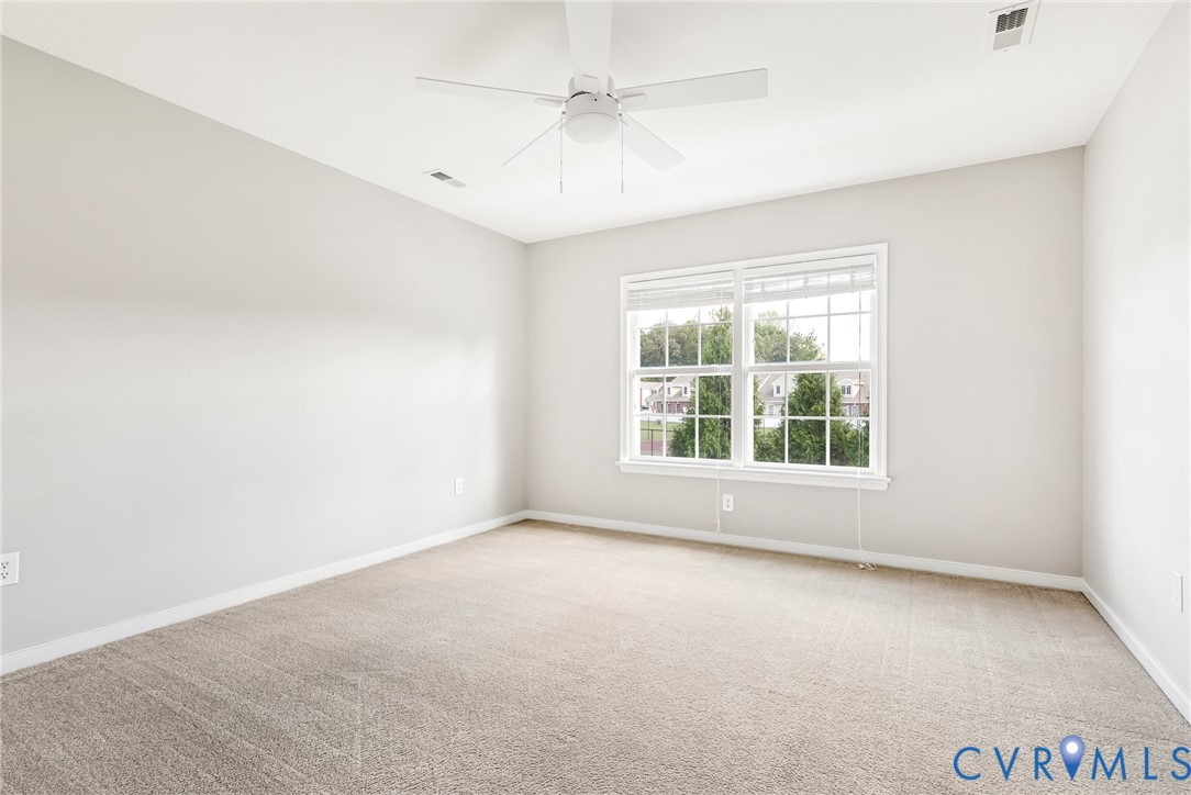 Room with light neutral wall paint, white ceiling fan, and carpeted flooring