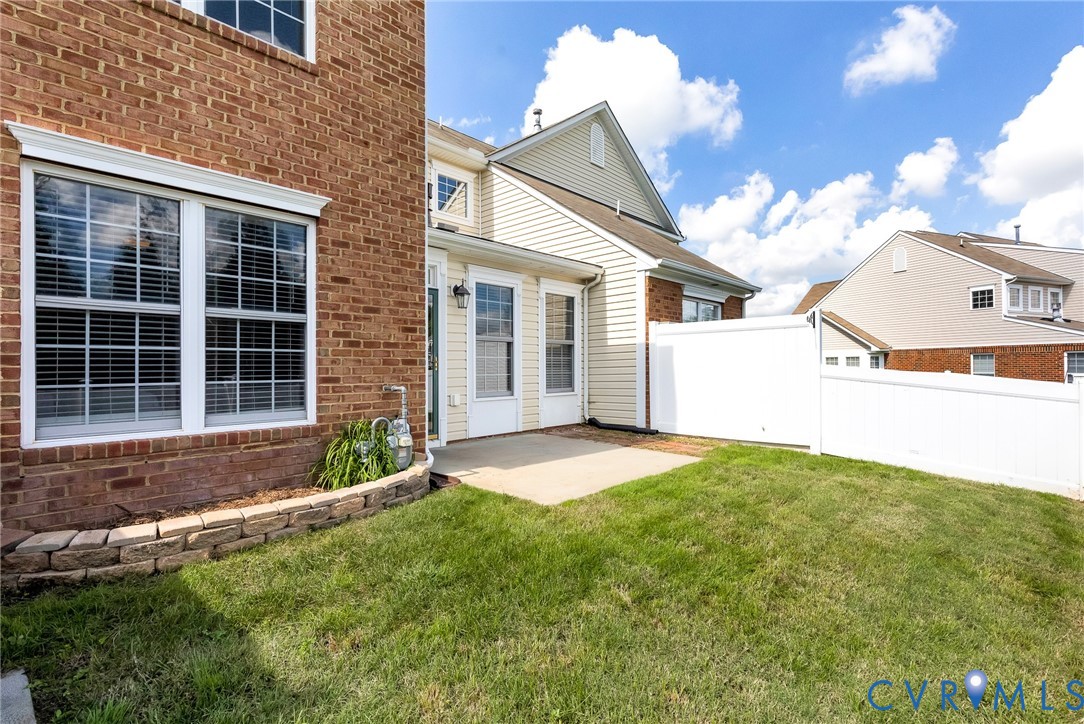 Brick and siding exterior, white vinyl fencing, concrete patio, stone retaining wall, and manicured lawn