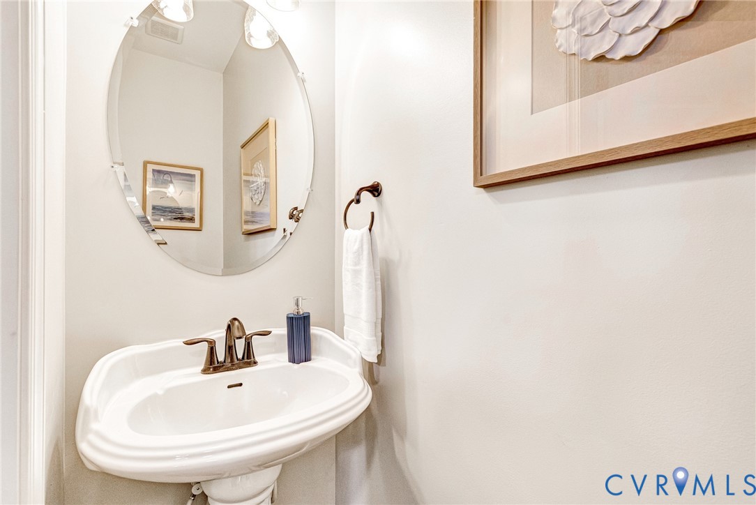 Pedestal sink with bronze-finish faucet, oval mirror with overhead sconce lighting, and a coordinating bronze-finish towel ring