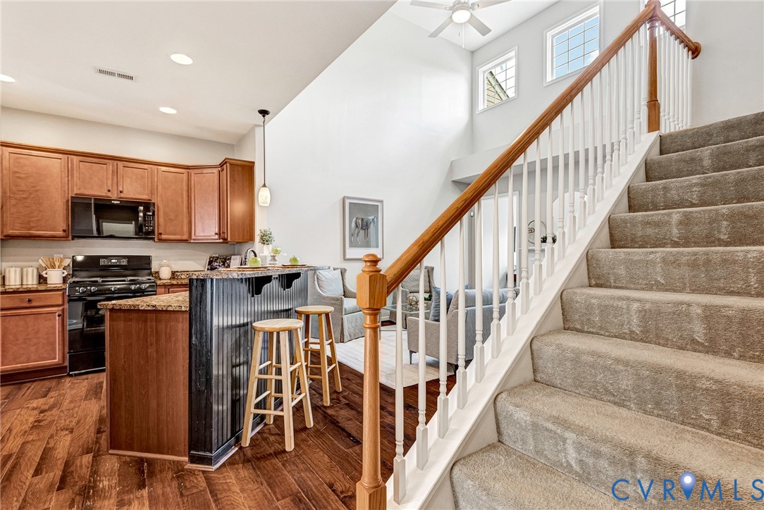Kitchen featuring warm wood cabinetry, black appliances, and a breakfast bar with stone-look countertop