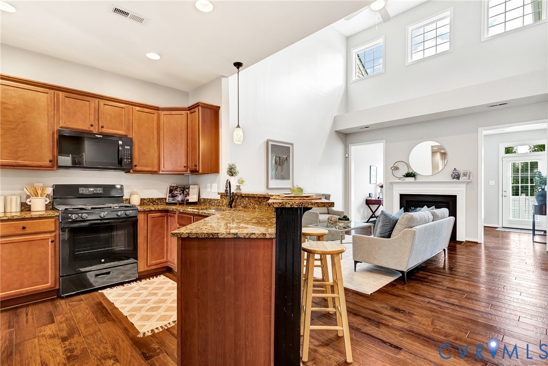 Open-concept kitchen featuring wood-finish cabinetry, black appliances, and granite countertops with a breakfast bar Open-concept kitchen featuring wood-finish cabinetry, black appliances, and granite countertops with a breakfast bar