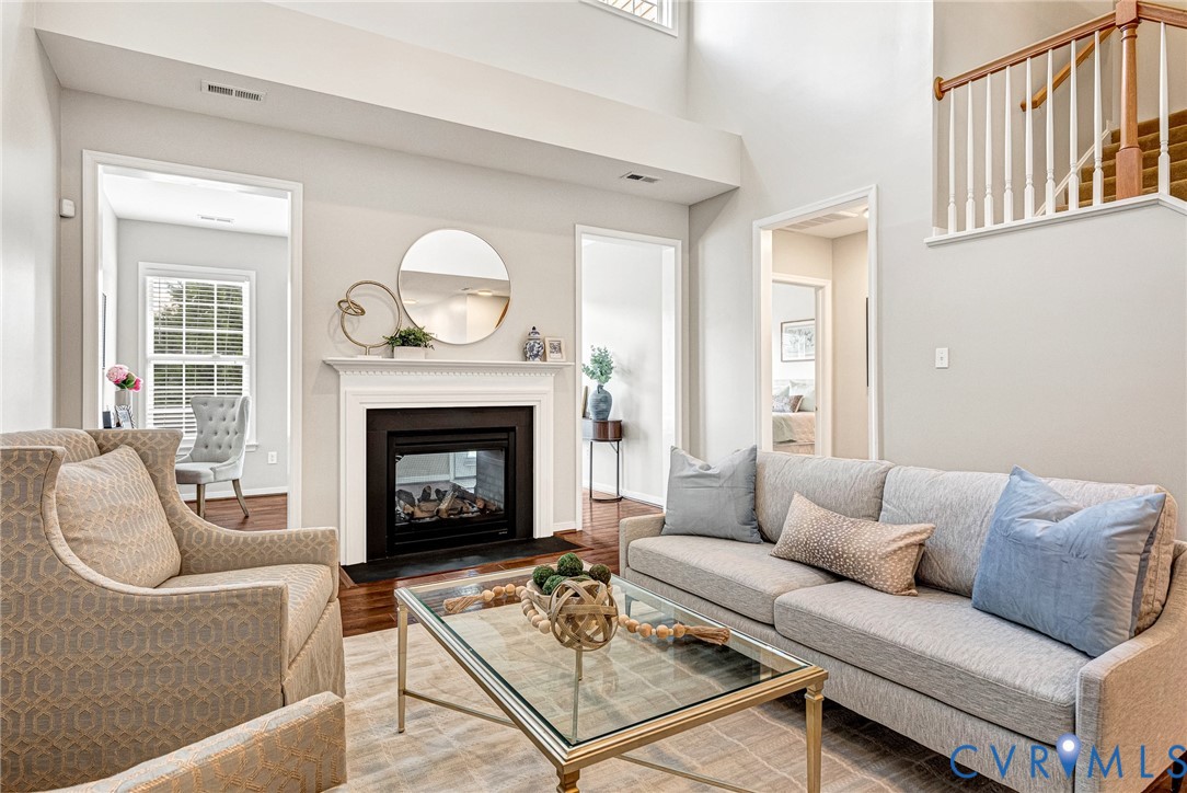 Living area featuring a white mantel fireplace with a black insert, high ceilings, wood-finish flooring, and a staircase with wood handrails and white balusters