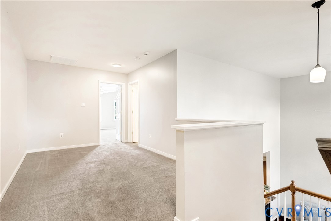Carpeted flooring throughout, recessed lighting, white walls, and a suspended pendant light