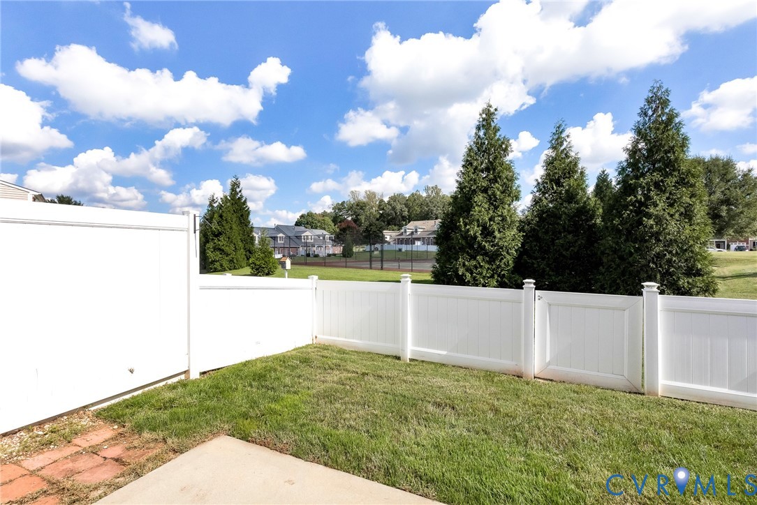 Enclosed backyard featuring a white privacy fence, concrete patio, and a brick paver pathway