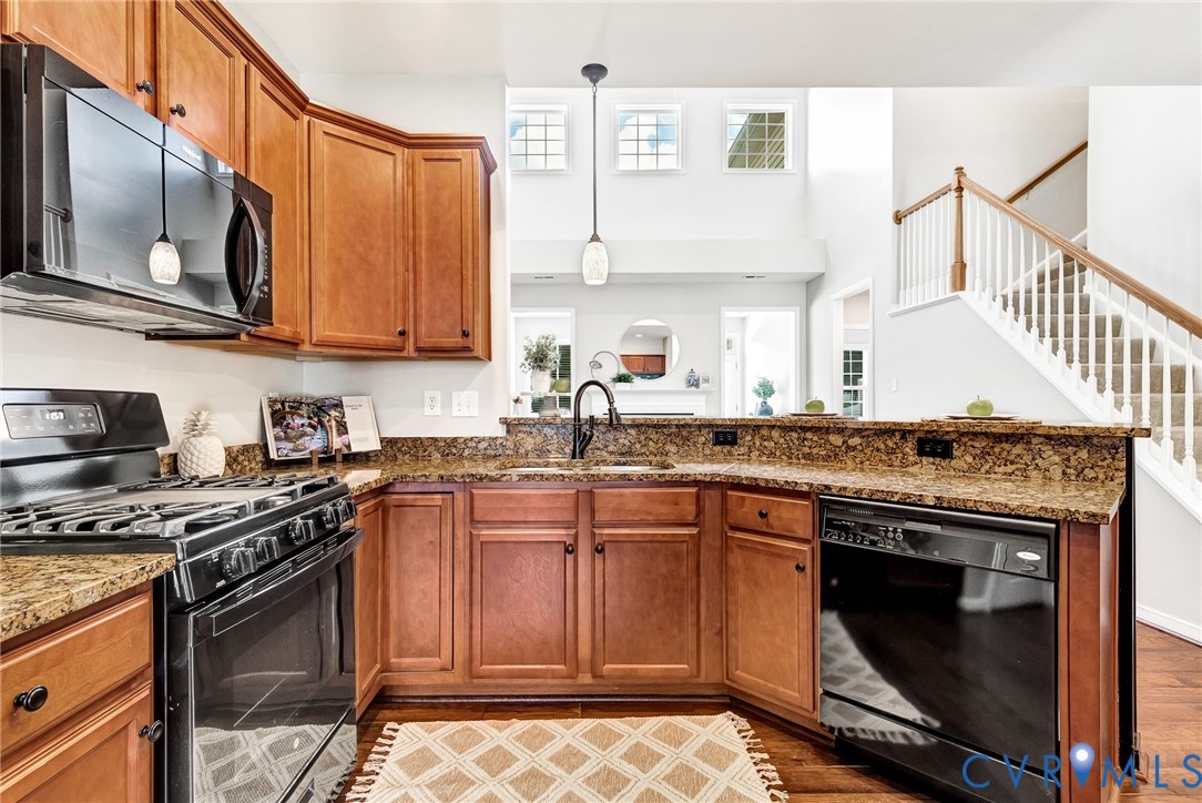 Kitchen featuring wood cabinetry, stone countertops, black appliances, and pendant lighting
