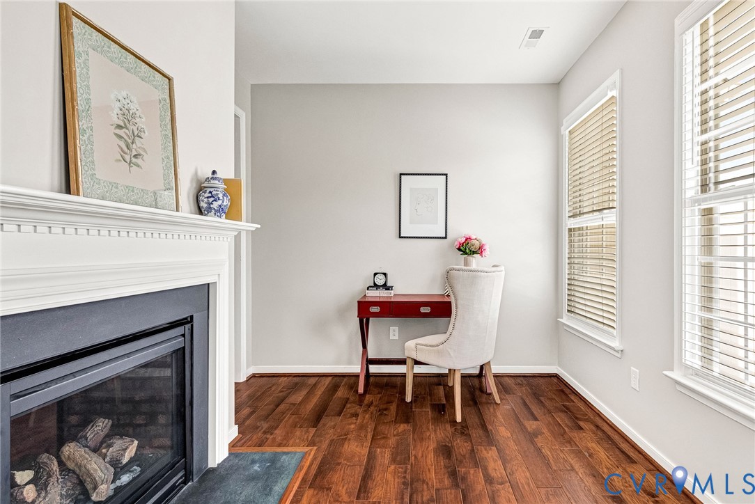 Hardwood-finish flooring, white trim, white walls, and a fireplace with a white mantel and dark hearth