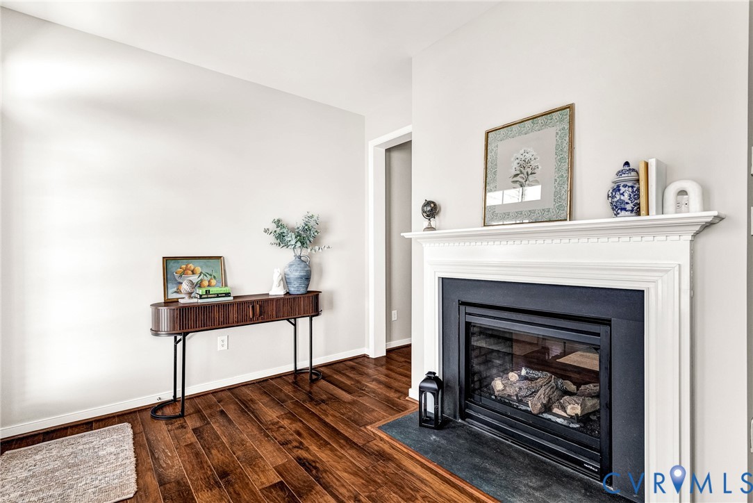 Hardwood flooring, white painted walls, white mantel, and a black fireplace insert with a stone hearth