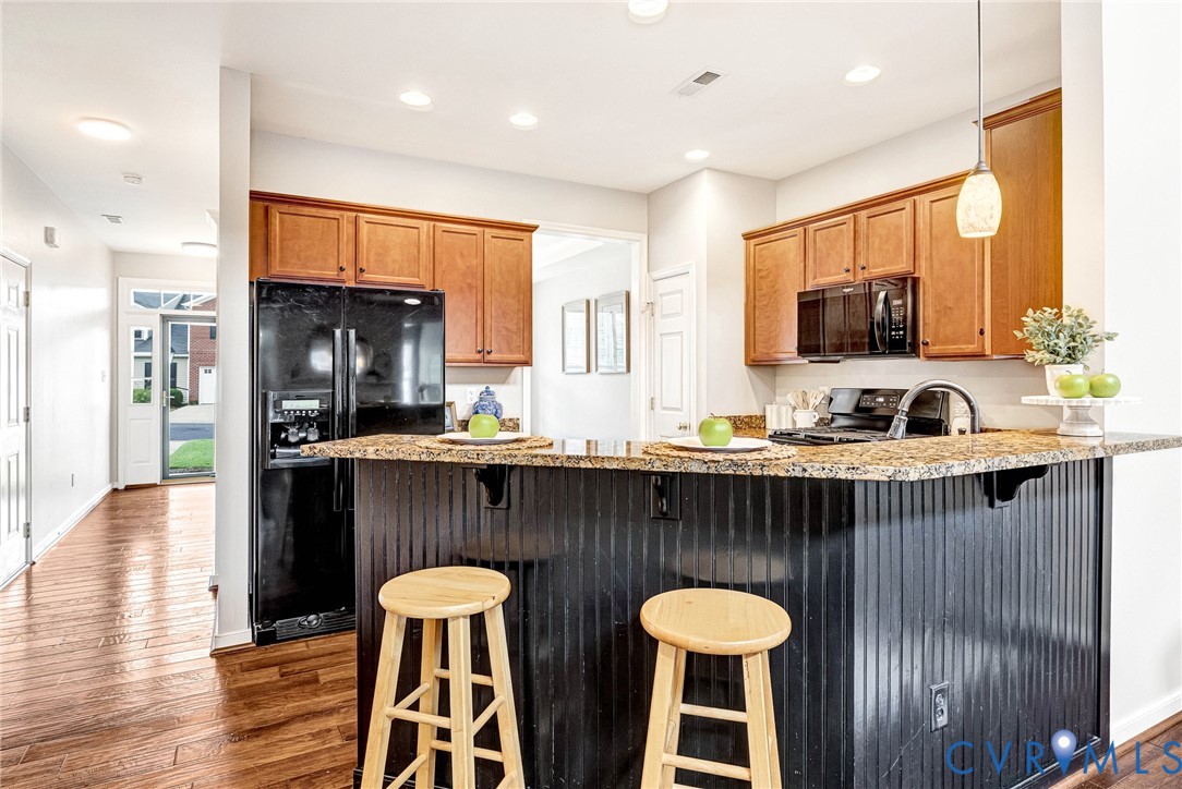 Kitchen featuring wood-finish flooring, granite-style countertops, wood cabinetry, built-in microwave, and black appliances