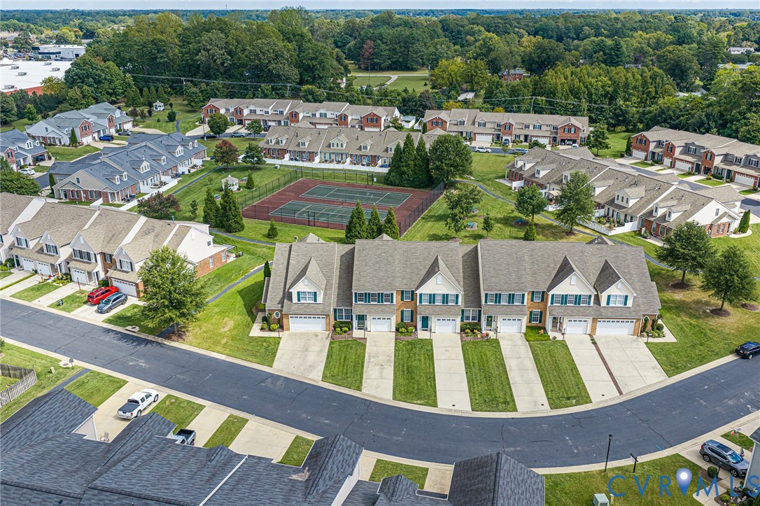 Community setting featuring multiple townhomes, mature trees, and a central tennis court