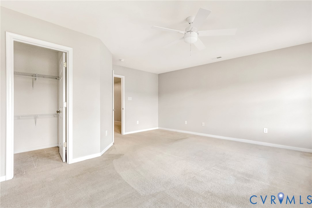Neutral wall paint, plush carpet flooring, ceiling fan, and wire shelving in a built-in closet