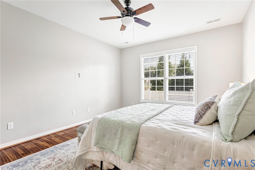 Wood-finish flooring with light-toned walls, a ceiling fan with light fixture, and a double window with blinds
