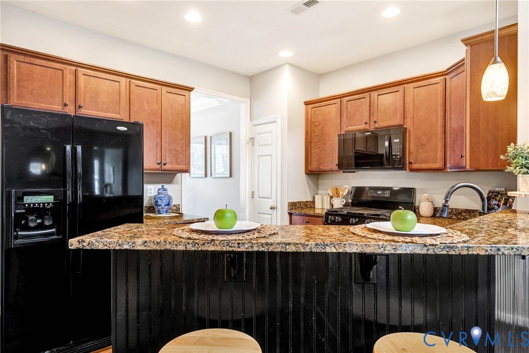 Kitchen featuring stone countertops, wood cabinetry, built-in microwave, black refrigerator, and black range