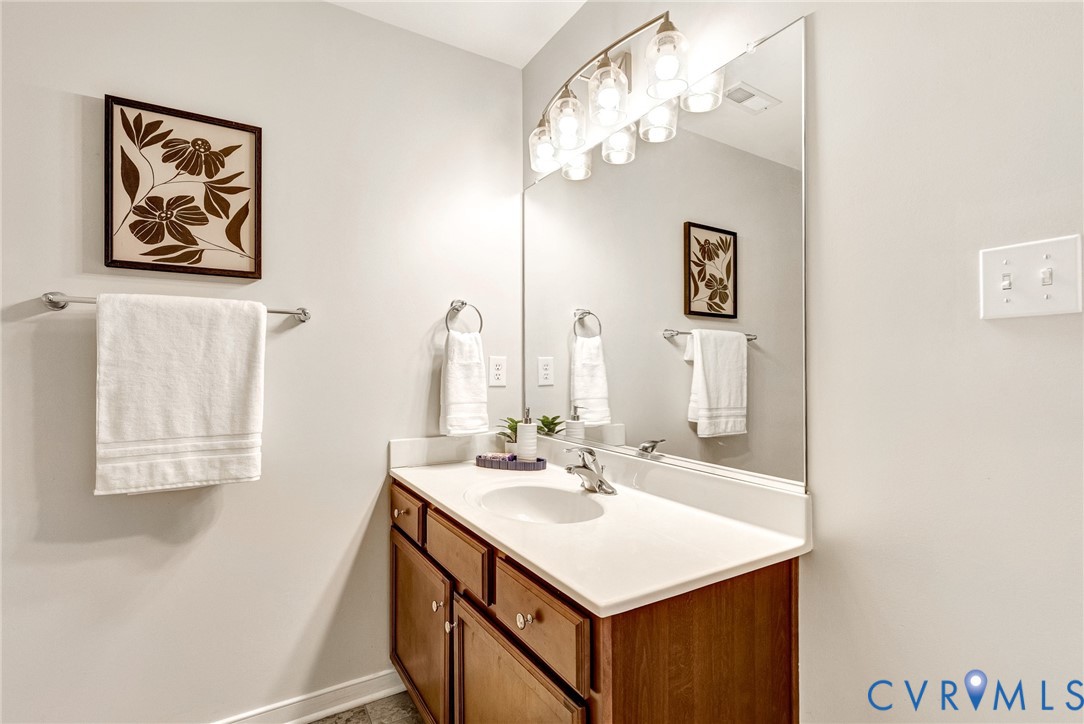 Single vanity with a light-toned countertop, integrated sink, and wood-finish cabinetry