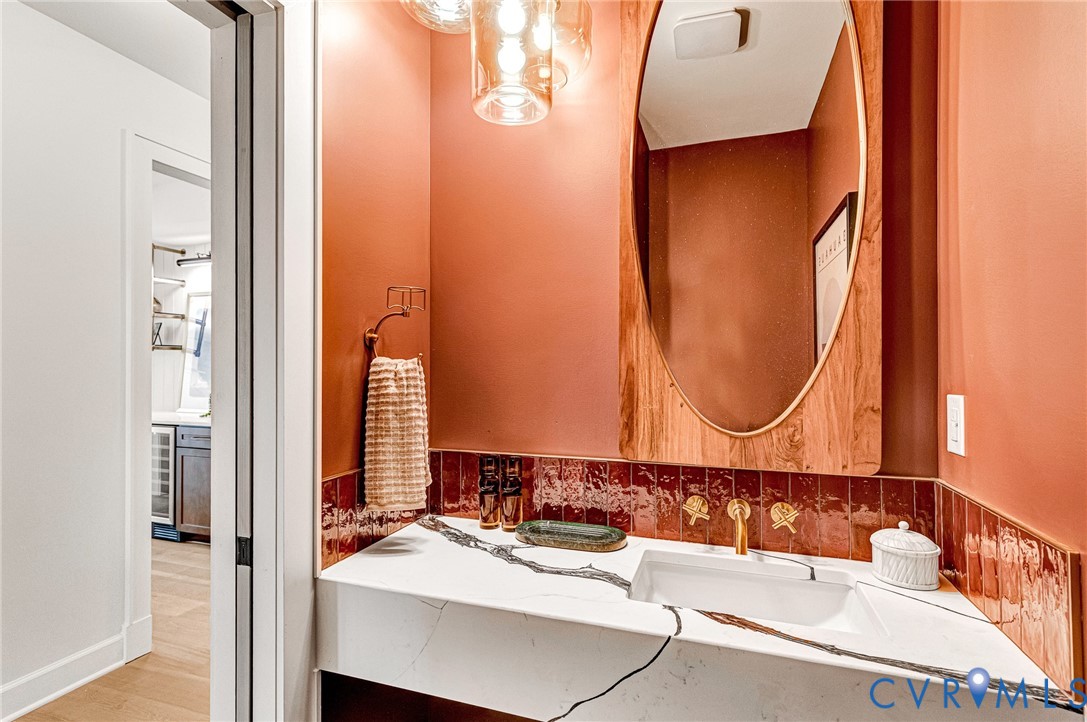 Floating vanity with a white composite countertop, rectangular basin, gold-toned faucet, warm-toned ceramic tile backsplash, and wood-framed oval mirror