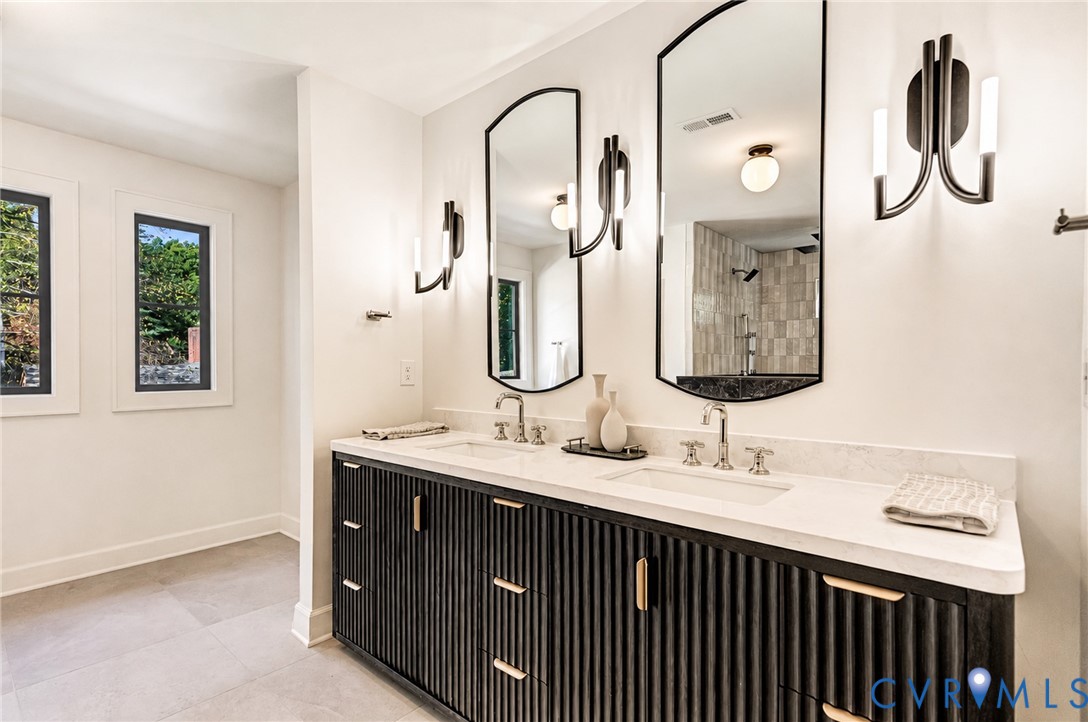 Dual-sink vanity featuring a fluted dark wood-finish cabinet, stone countertop, arched wall-mounted mirrors, and contemporary multi-arm light fixtures